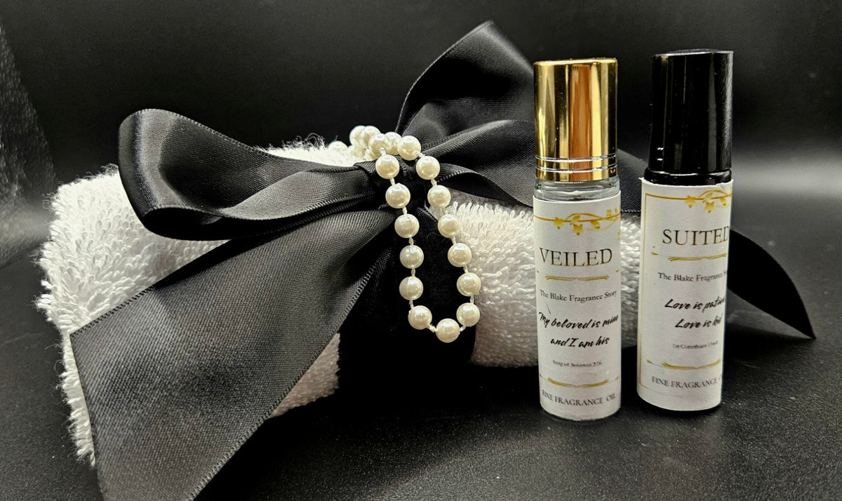 Veiled and Suited fragrance rollers presented together with a black satin bow, pearls, and white washcloth